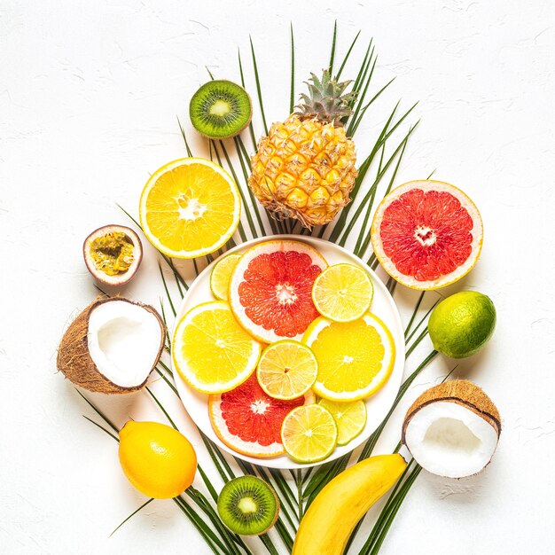 Tropical fruits and palm leaves on a white background, top view.