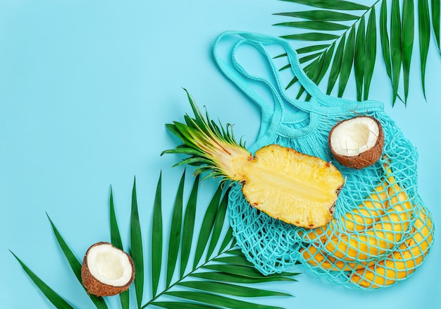 Тропические фрукты и многоразовая хлопковая сумка на синем летнем фоне. Скопируйте пространство, накладные расходы.