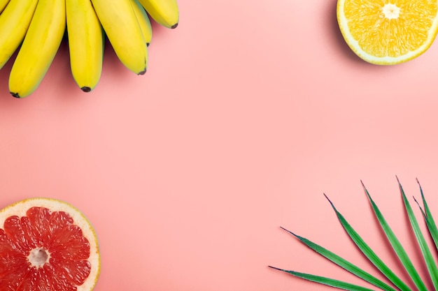 Tropical fruits summer background. Bananas, oranges and grapefruits on a colored pink background.