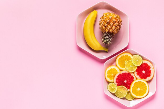 Tropical fruits whole and slices on plates, top view.