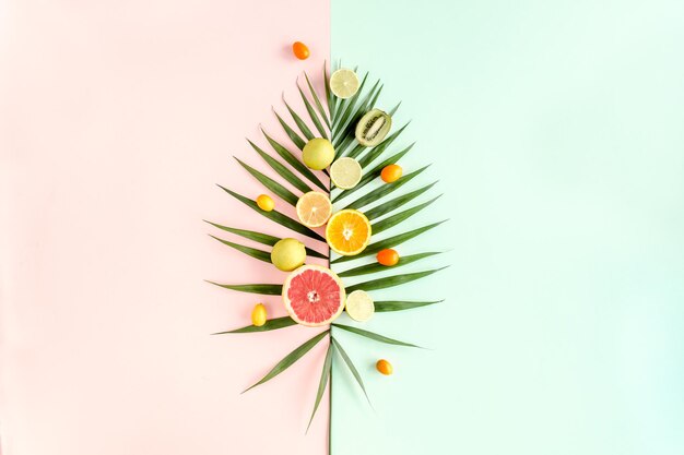 Tropical layout made of green palm leaf and fruits on colorful background food concept flat lay top