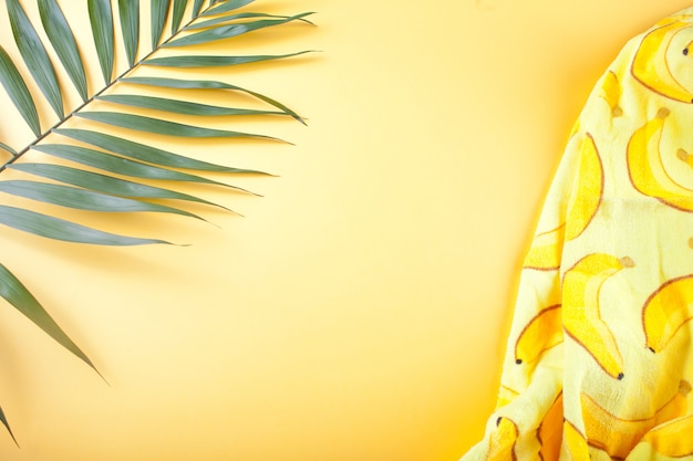 Фото Тропические листья и пляжное полотенце на желтой стене.