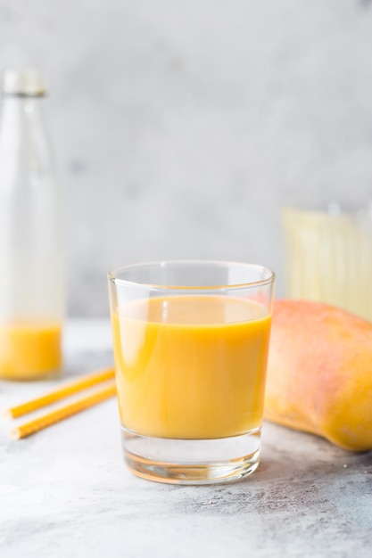 Tropical Mango smoothie in a glass and fresh mango on a light background. Mango shake. Tropical fruit concept.