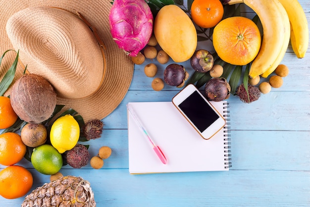 Tropical palm leaves, hat, many fruits on blue wooden background. 