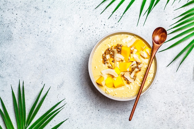 Tropical smoothie bowl with mango, passion fruit and coconut, light background.