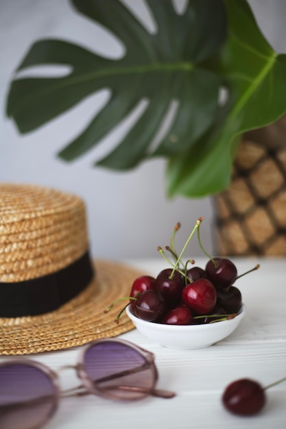Tropical still life with straw hat cherries green plants and sunglasses
