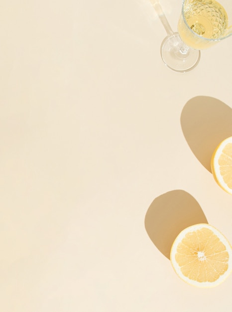 Foto concetto creativo estivo tropicale con limone fresco e bicchiere di vino, con ombre su sfondo soleggiato. posa piatta minima. sfondo minimo con copia spazio