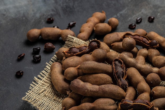 Tropisch fruit Tamarindo bonen in dop op een bruin slagersblok op een donkere achtergrond gezond fruit banner menu recept plaats voor tekst bovenaanzicht