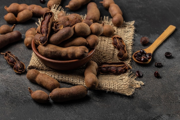 Tropisch fruit Tamarindo bonen in dop op een bruin slagersblok op een donkere achtergrond gezond fruit banner menu recept plaats voor tekst bovenaanzicht