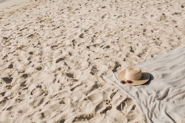 Tropisch mooi strand met wit zand, voetstappen, neutrale deken met strohoed en zonnebril