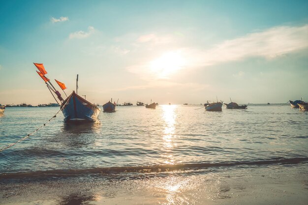 Tropisch zeegezicht met een boot op zandstrand bij bewolkte zonsopgang of zonsondergang Prachtige zonsondergang tropisch strand met kleine boot en filmische hemel voor reizen en vakantie in vakantie ontspannen tijd