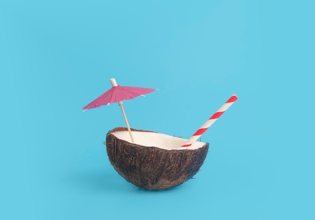 Tropisch zomer- en vakantie minimaal concept. Kokosnoot op een blauwe achtergrond met een cocktailstro. Vakantie, reizen, strandidee.