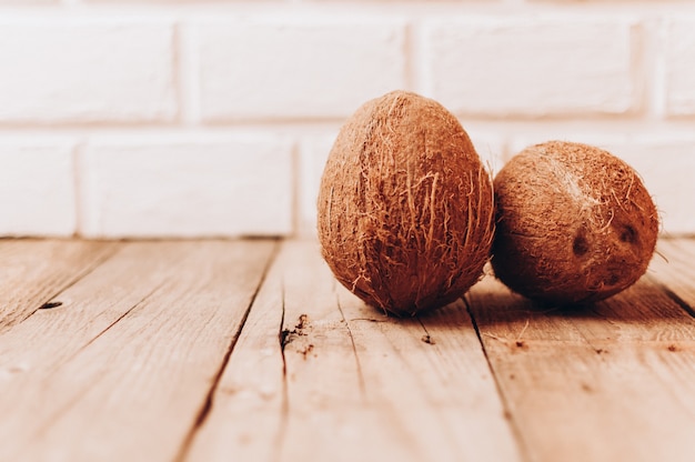 Tropische kokosnotenvruchten op een houten lijst tegen een bakstenen muurachtergrond.