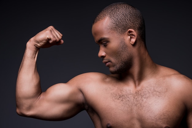 Trots op zijn perfecte biceps. Jonge, shirtloze Afrikaanse man die naar zijn biceps kijkt