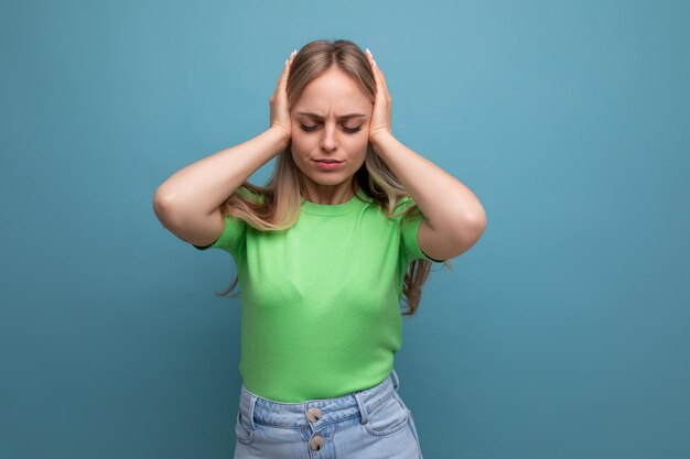 Trotse blonde jonge vrouw bedekte haar oren met haar handen op een blauwe geïsoleerde achtergrond