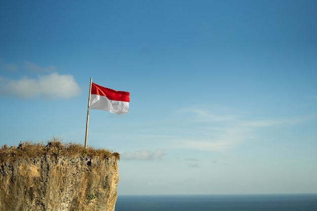 Trotse Indonesische man op een strandklif die de rode en witte vlag van Indonesië opheft