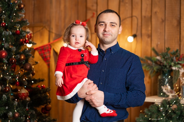 Trotse vader met zijn dochtertje in zijn armen naast de kerstboom