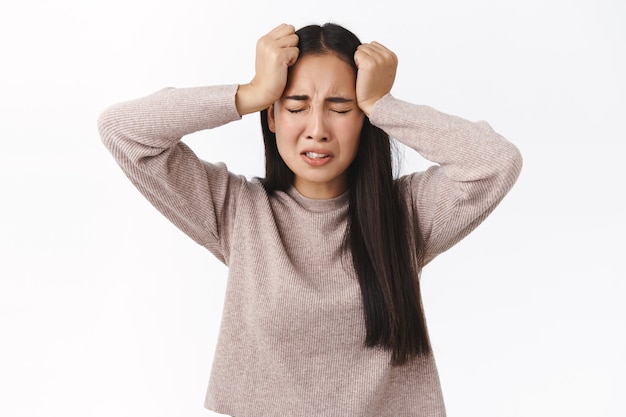 Troubled asian girl cant understand what happening, need help, suffering emotional breakdown, close eyes and grab head, crying feeling distressed and upset