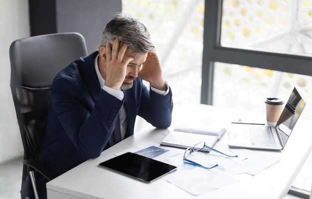 Troubles at work stressed mature businessman sitting in office and touching head