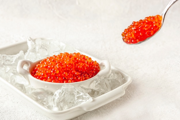 Trout caviar in a white bowl with ice on a white surface