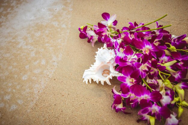 Trouwringen in een schelp op het strand met bloemen