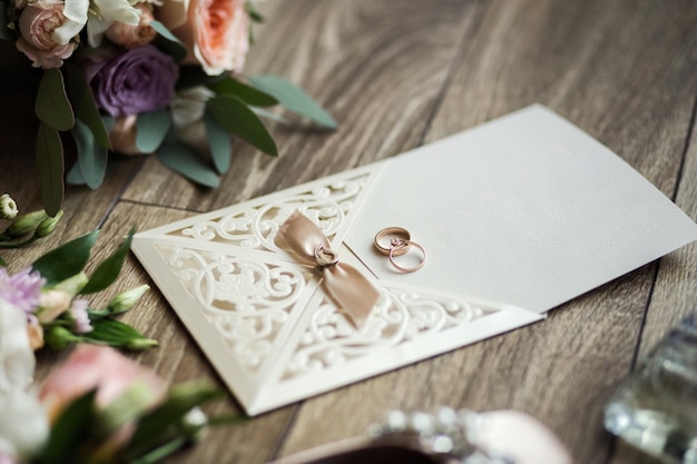 Foto trouwringen liggen op de uitnodigingskaart op de achtergrond van een boeket