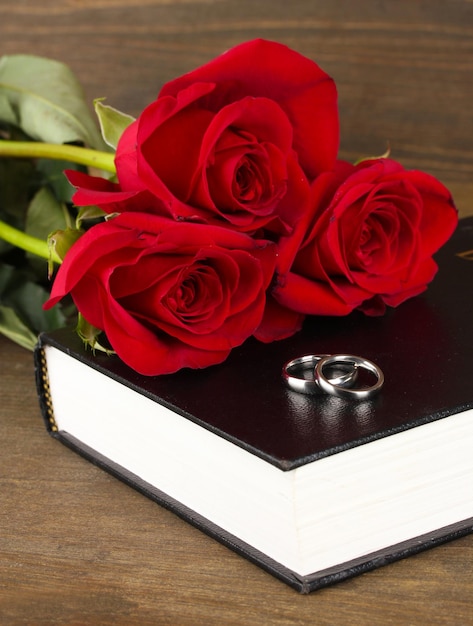 Trouwringen op bijbel met rozen op houten achtergrond