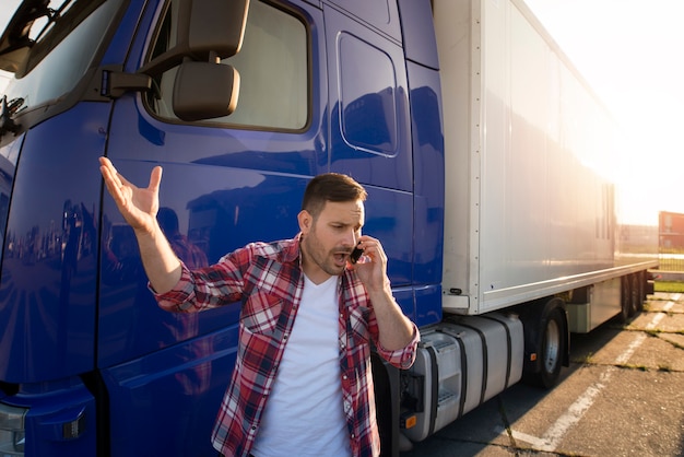 電話で話し、トラックのトレーラーの前で議論しているトラックの運転手。