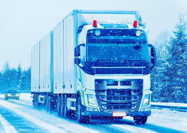 Truck in snow winter road of Finland. Trucker in highway. Lorry doing logistics work. Semi trailer with driver. Big cargo car drive. Freight delivery. Transport export industry. Container with goods