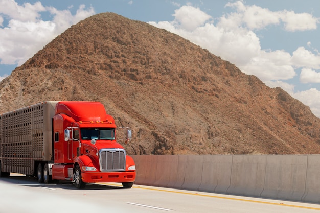 写真 山を背景に高速道路で動物を輸送するためのトレーラーが付いているトラック。貨物のコンセプト。