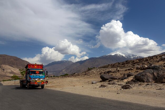 A truck with a red roof drives down a road with mountains in the background.