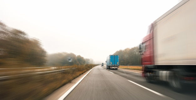 Camion che guidano sull'autostrada girando verso l'orizzonte in un paesaggio autunnale con nebbia, copyspace per il tuo testo individuale.