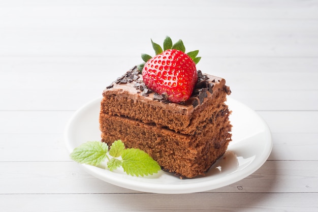 Truffelcake met chocolade en aardbeien en munt op een witte houten lijst.