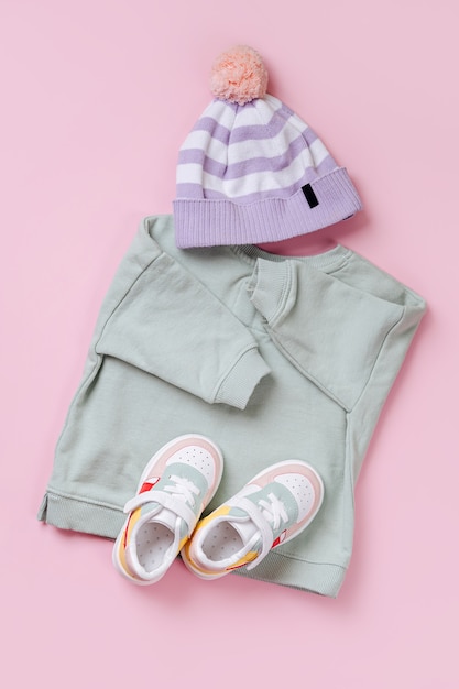 Trui en muts met sneakers. Set babykleding en accessoires voor lente, herfst of zomer op roze achtergrond. Mode kinderoutfit. Platliggend, bovenaanzicht