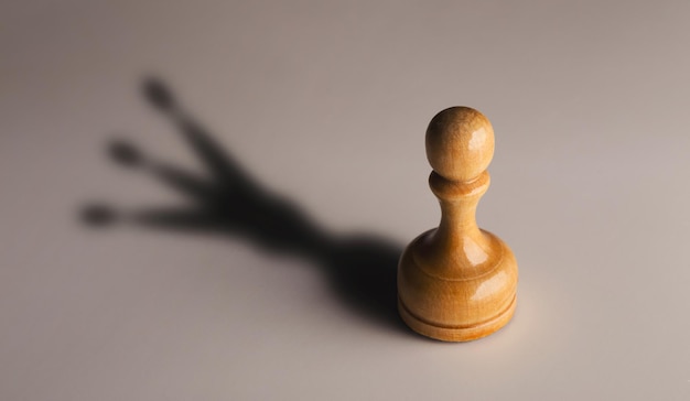 Trust yourself, self confidence concept. Wooden chess pawn with king shadow on gray background, motivation poster