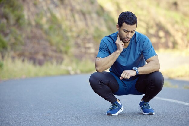 Trying to bring my heart rate back down Full length shot of a handsome young man crouching and timing his pulse during his outdoor workout