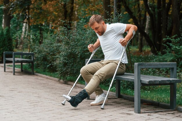 写真 立ち上がろうとしている松葉杖をついた男性が屋外の公園にいる足に怪我をしている