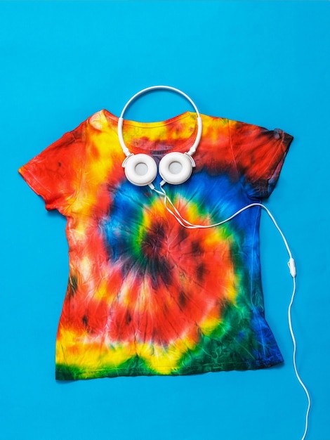 Photo tshirt with a spiral tie dye pattern and headphones on a blue background flat lay pastel color