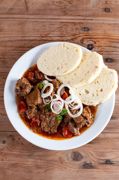 Tsjechische traditionele goulash met gepaneerde knoedel en ui op witte plaat op tafel