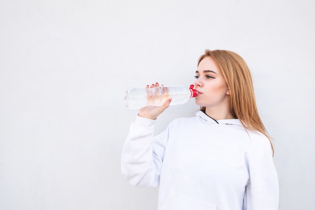 La ragazza di ttractive che porta l'abbigliamento sportivo beve le bottiglie di acqua