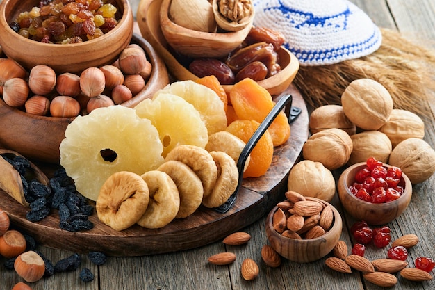 Tu Bishvat celebration concept Mix of dry fruits and nuts almonds hazelnuts walnuts apricots prunes cherries raisins dates apples figs over wooden table Jewish holiday new year of trees