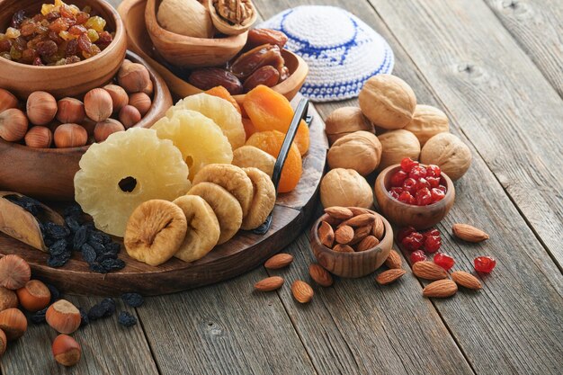 Tu Bishvat celebration concept Mix of dry fruits and nuts almonds hazelnuts walnuts apricots prunes cherries raisins dates apples figs over wooden table Jewish holiday new year of trees