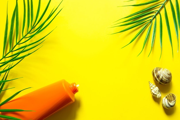 Tube zonnebrandcrème op een gele zomerachtergrond met palmbladeren en de zon. Bruiningsmiddel, huidbescherming, een reis naar de zee, vakantie op het strand, UV-bescherming, SPF-filter. Plat leggen, ruimte kopiëren