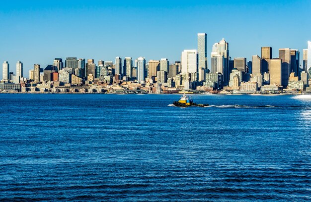 A tug boat moves across the port of seattle with the skyline in the distance
