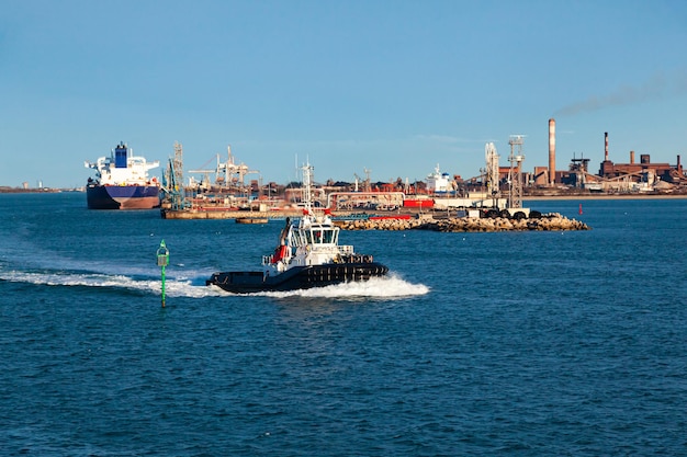 Tug boat sailing in bay of seaport of FossurMer France with cranes and wind generators on the coast