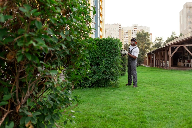 Tuinier in uniform snijdt struiken. Afro-Amerikaanse man met een bril werkt in de tuin.