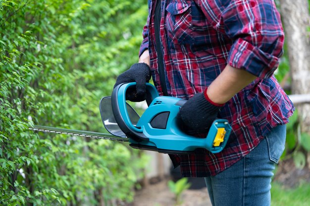 Tuinier met een elektrische hegtrimmer om de boomtop in de tuin te snijden Hobby planten thuis tuin