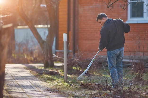 Tuinman die dalingsbladeren in tuin harken. Kopieer ruimte.