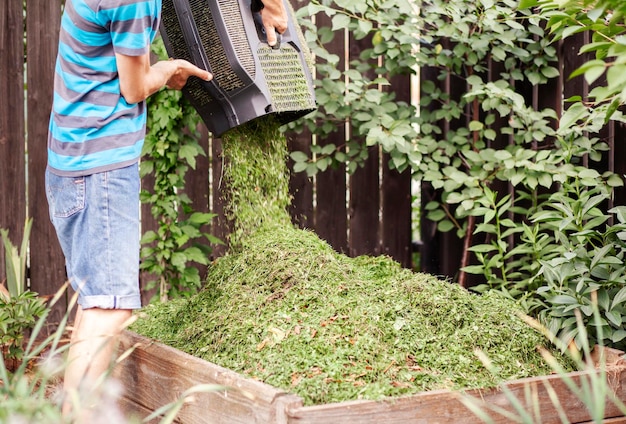 Tuinman gooit gras van de grasmaaier in de compostbak in de tuin en bereidt compostrecyclingafval voor