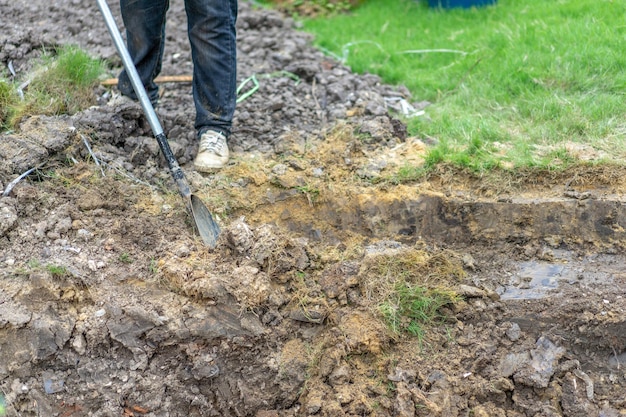 Tuinman graaft de grond met zijn uitrusting om te tuinieren en maakt land klaar voor plantage.